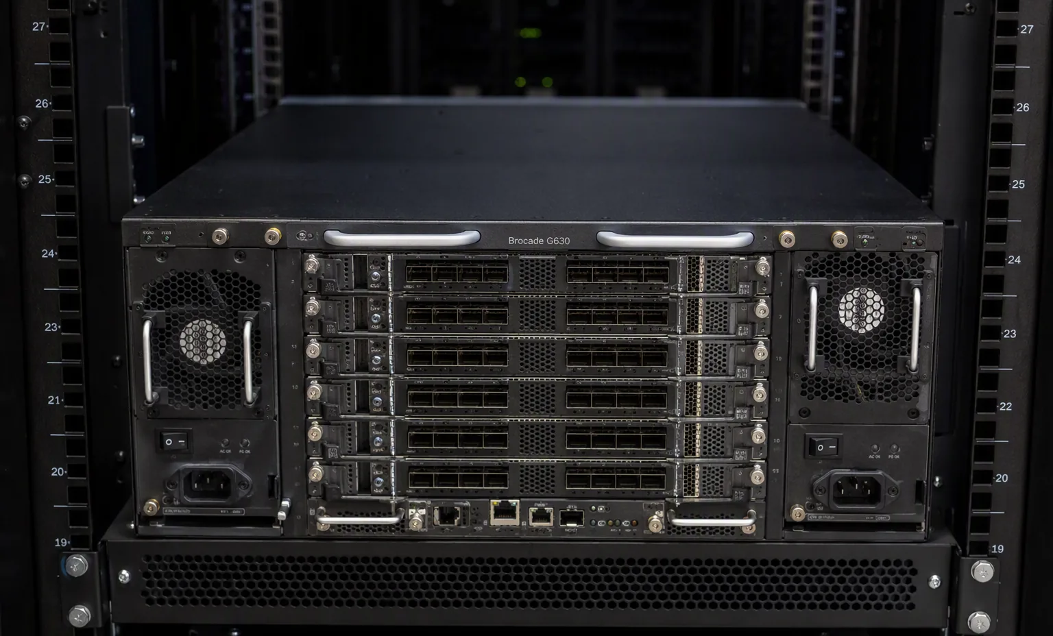 rear panel of a Brocade G630 SAN director, dual hot-swap PSU and fan modules, port blades visible, accurate 4U chassis layout, dark data center.