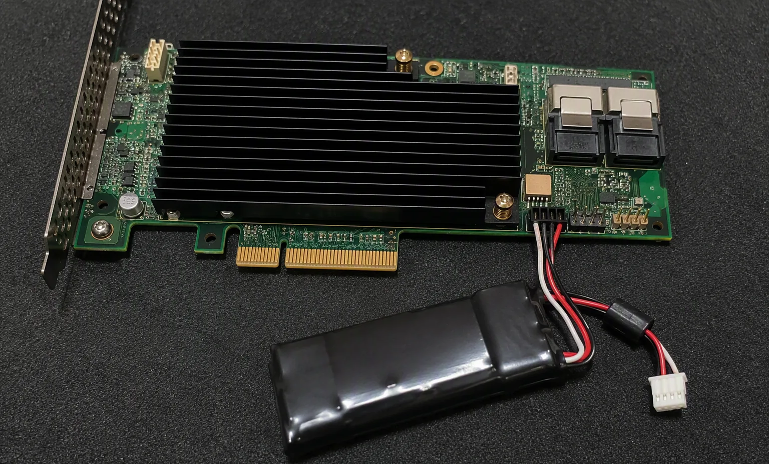 RAID controller cache backup battery module and cable on dark anti-static mat, macro shot.