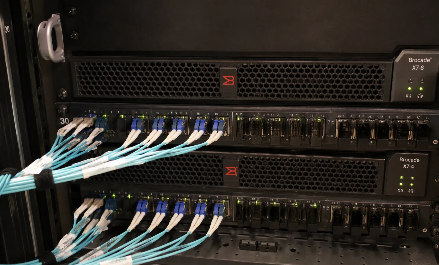 fiber channel cabling with LC connectors patched into a Brocade SAN switch, close-up, dark rack.